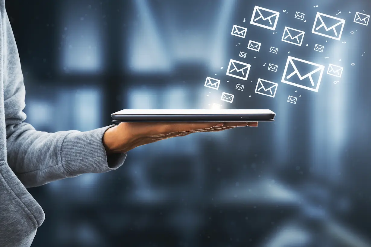 Close-up of a hand holding a tablet, with digital email icons floating above it, symbolizing email marketing for real estate business and communication.